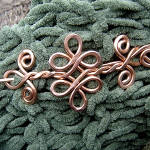 May include: A copper wire hair pin with a decorative knot design. The pin is on a green fuzzy surface.