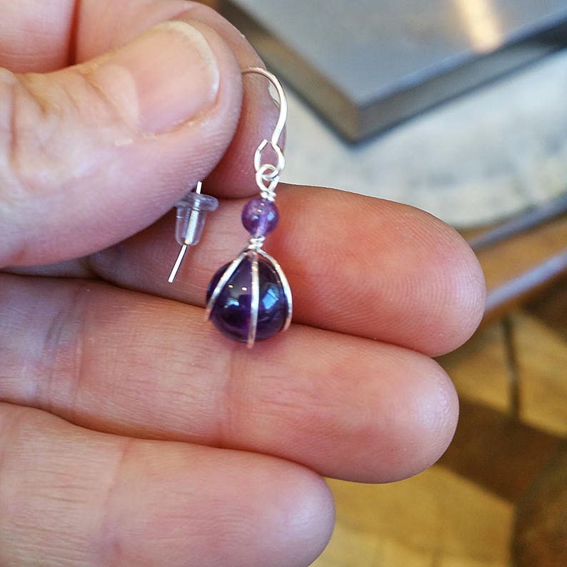 May include: A silver wire wrapped amethyst gemstone dangle earring with a purple bead.