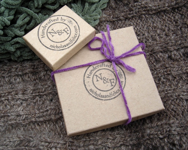 May include: Two brown cardboard boxes with a purple ribbon on one. Both boxes have a round stamp that says "Handcrafted by N&F nicholasandfelice.com".
