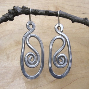 May include: A pair of silver metal earrings with a unique, abstract design. Each earring features a swirl pattern within a larger oval shape.