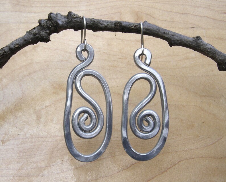 May include: A pair of silver metal earrings with a unique, abstract design. Each earring features a swirl pattern within a larger oval shape.