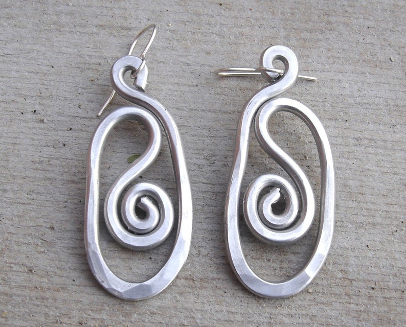 May include: A pair of silver earrings with a unique design. Each earring features a large oval shape with a smaller spiral inside. The earrings are made of metal and have a polished finish.