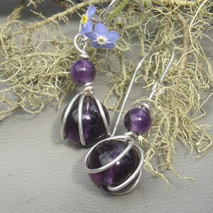 May include: A pair of silver earrings with purple amethyst stones. The stones are encased in a wire cage design.