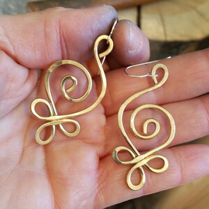 May include: A pair of gold-toned wire earrings with a swirling, abstract design. The earrings are handmade and have a delicate, feminine look.