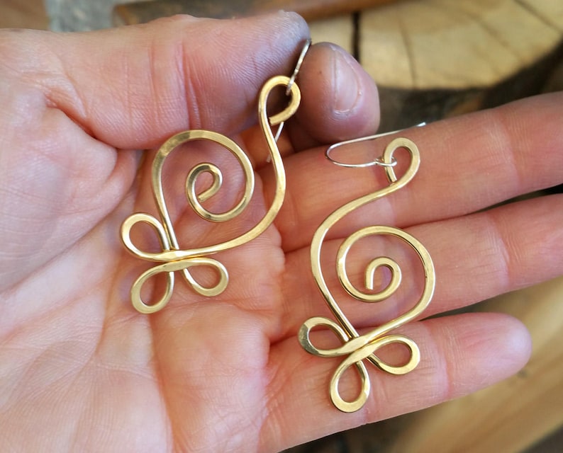 May include: A pair of gold-toned wire earrings with a swirling, abstract design. The earrings are handmade and have a delicate, feminine look.