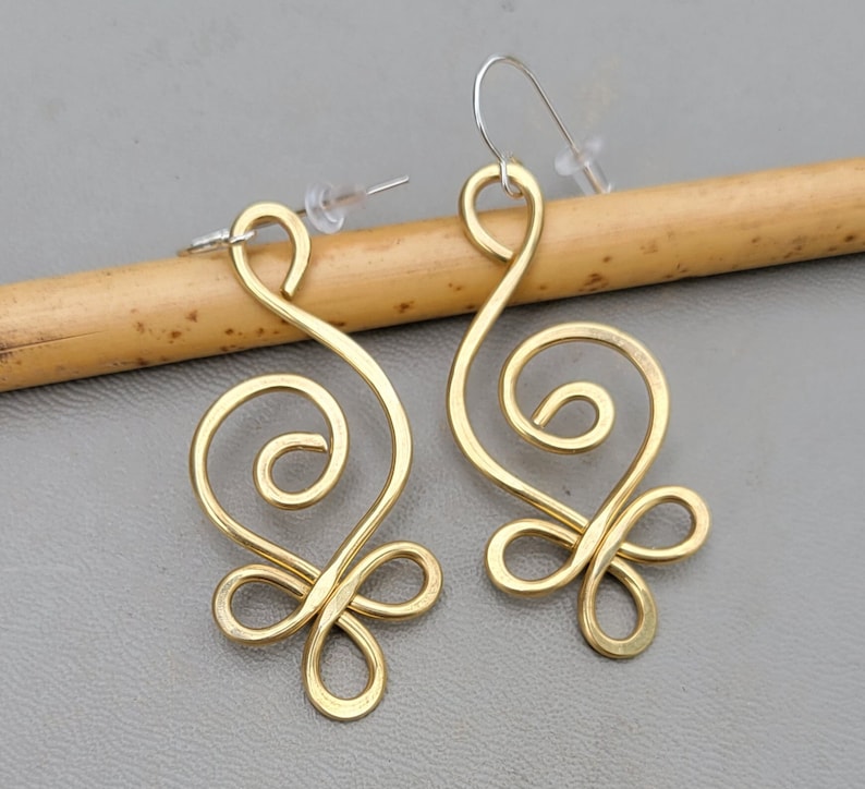 May include: A pair of gold-tone earrings with a swirling, abstract design. The earrings are made of wire and have a delicate, feminine look.