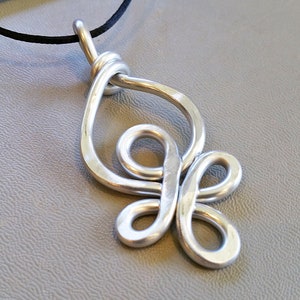 May include: A silver metal pendant necklace with a unique, intricate design. The pendant features a series of interconnected loops and curves, creating a flowing, abstract shape.