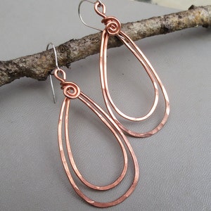 May include: A pair of copper teardrop earrings with a hammered finish. The earrings are double-layered and have a wire wrapped detail at the top.