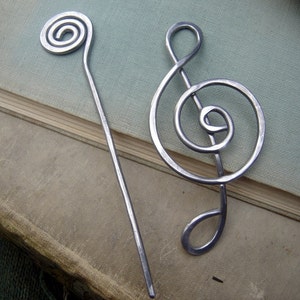 May include: Two silver metal hair pins. One is a simple spiral and the other is shaped like a treble clef.
