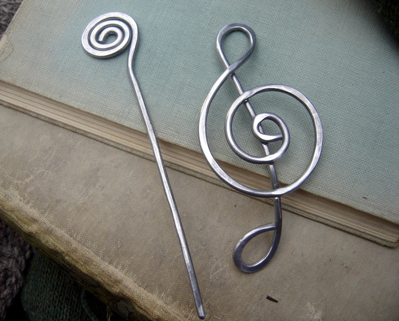 May include: Two silver metal hair pins. One is a simple spiral and the other is shaped like a treble clef.