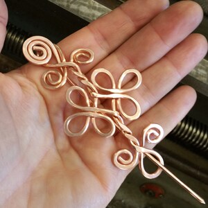 May include: A copper wire hair stick with a decorative design of intertwined loops and swirls. The stick is about 6 inches long and has a pointed end.