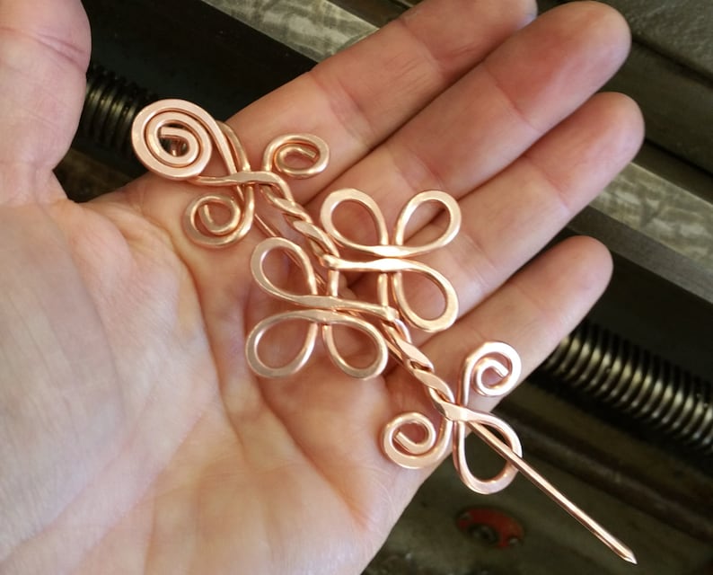 May include: A copper wire hair stick with a decorative design of intertwined loops and swirls. The stick is about 6 inches long and has a pointed end.