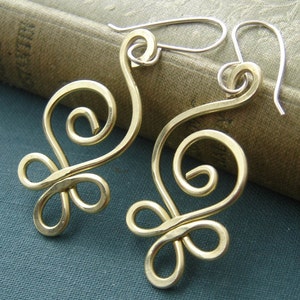 May include: A pair of gold-toned earrings with a delicate, swirling design. The earrings are made of wire and have a simple, elegant look.