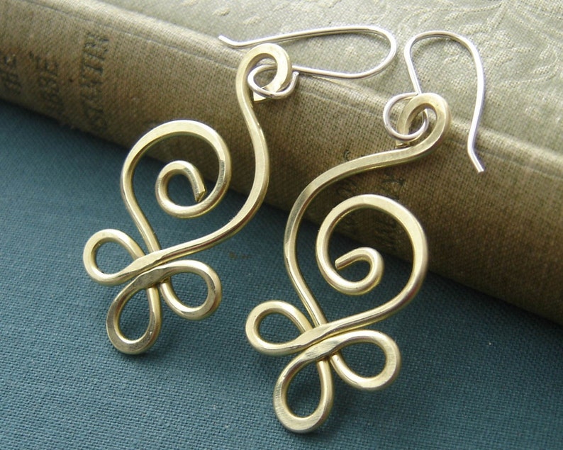 May include: A pair of gold-toned earrings with a delicate, swirling design. The earrings are made of wire and have a simple, elegant look.