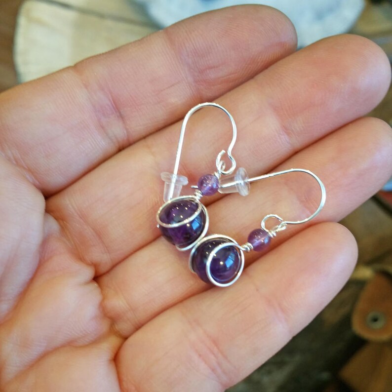May include: A pair of silver wire wrapped earrings with amethyst gemstones. The earrings are made with two amethyst beads on each earring, and the wire is wrapped around the beads to create a secure and stylish look.