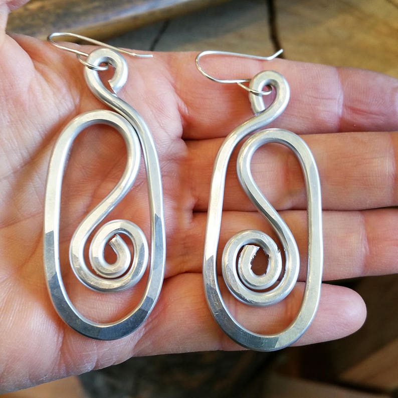 May include: A pair of silver dangle earrings with a unique swirl design. The earrings are made of metal and have a simple, elegant look.