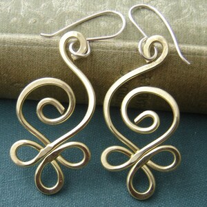 May include: A pair of gold-toned earrings with a swirling, abstract design. The earrings are made of wire and have a delicate, feminine look.