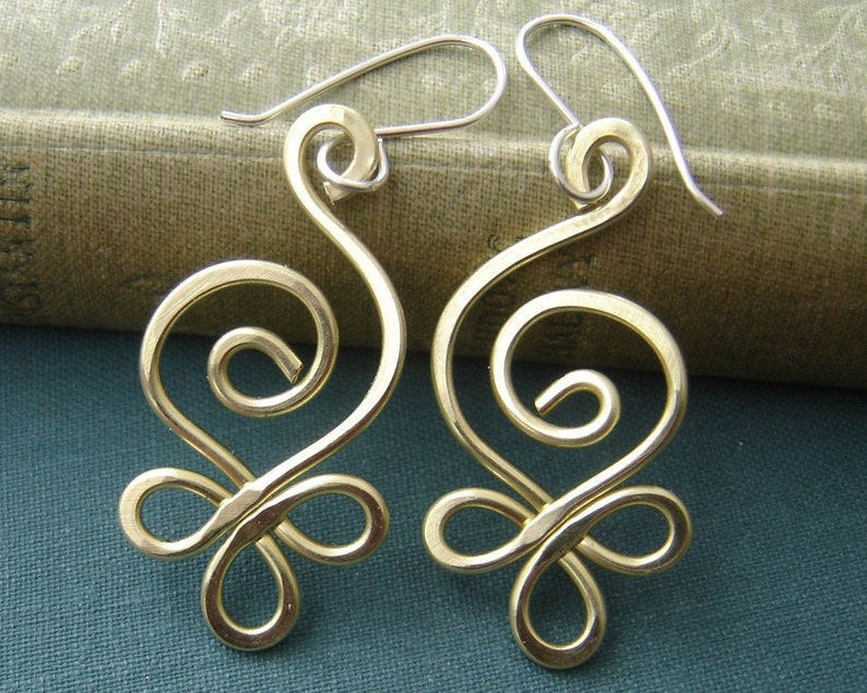 May include: A pair of gold-toned earrings with a swirling, abstract design. The earrings are made of wire and have a delicate, feminine look.