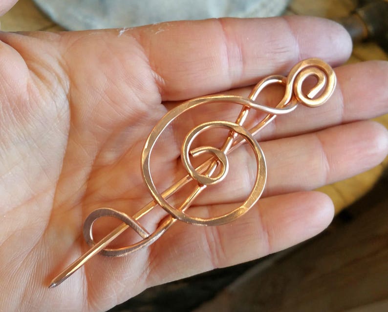 May include: A copper-colored treble clef hair stick. The stick is made of wire and is shaped like a treble clef. It is about 6 inches long.