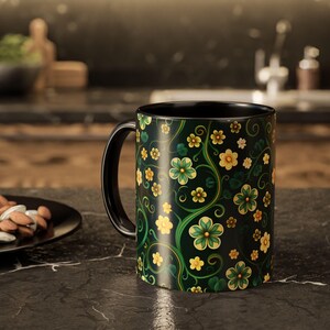 Puede incluir: Taza de cerámica negra con un diseño floral. El diseño presenta flores amarillas y verdes con enredaderas verdes sobre un fondo oscuro. El interior y el asa de la taza son negros.