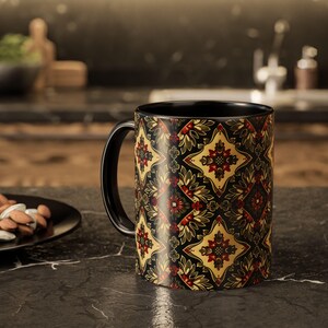 Puede incluir: Taza de cerámica negra con un patrón decorativo en dorado, rojo y verde. El diseño presenta formas florales y geométricas. La taza tiene un asa e interior negros, adecuada para bebidas calientes.