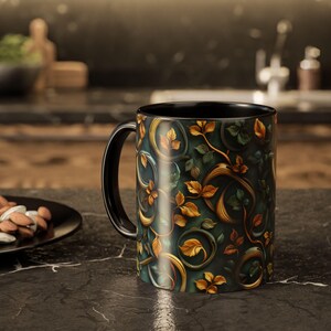 Puede incluir: Una taza de café negra con un diseño botánico detallado con hojas y vides doradas y verdes sobre un fondo verde oscuro. La taza tiene un asa e interior negros.