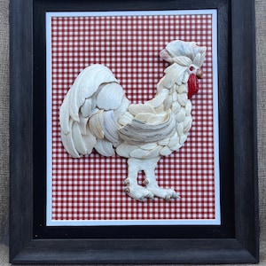 Puede incluir: Un gallo blanco hecho de conchas marinas se muestra sobre un fondo de cuadros rojos y blancos. El gallo está enmarcado en un marco negro.
