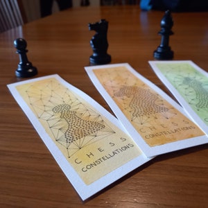 Peut inclure: Trois marque-pages aquarelle avec un motif de pièce d'échecs. Chaque marque-page présente un dégradé de couleur différent et un motif géométrique noir et blanc d'une pièce d'échecs. Les marque-pages portent le texte "Chess Constellations" imprimé dessus.