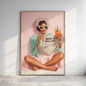 May include: A framed print of a woman in a vintage style, wearing sunglasses, a headscarf, and a pearl necklace. She holds a newspaper with the text "Better Late Than Ugly" and a cocktail. The artwork has a pink and teal color scheme.