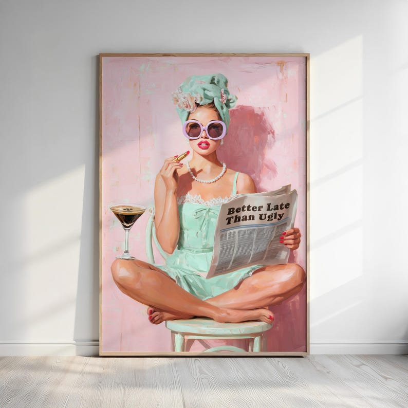 May include: A framed artwork depicts a woman in a mint green dress and head wrap, wearing large sunglasses and applying lipstick. She sits cross-legged, holding a newspaper with the text "Better Late Than Ugly" and a cocktail.