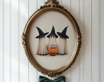 May include: An oval-shaped gold ornate frame containing an illustration of three white ghosts wearing black pointed witch hats. The center ghost holds a small orange jack-o'-lantern bucket. A dark green ribbon bow is attached to the bottom frame.