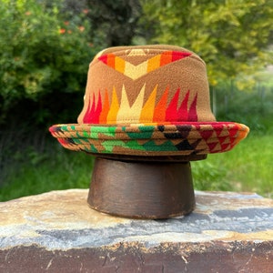 May include: A brown and multi-colored patterned bucket hat with a geometric design. The hat is made of a soft, woven fabric and has a wide brim.