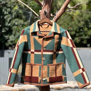 May include: A green, brown, and red plaid jacket with a button-up front and two patch pockets. The jacket is hanging on a wooden hanger against a blurred background of trees and a pool.