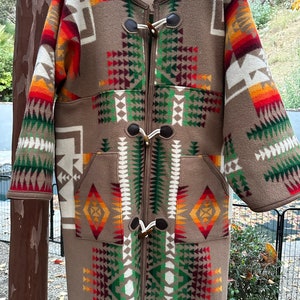 May include: A brown, long-sleeved coat with a geometric pattern in shades of red, orange, yellow, green, and white. The coat has a toggle closure and two pockets. The label on the coat reads "Campbel Cloth Co."