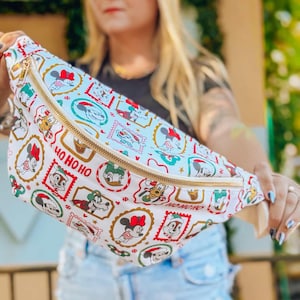 May include: White fanny pack with a gold zipper and a festive Disney character print. The print features Mickey Mouse, Minnie Mouse, Donald Duck, and Goofy in holiday-themed designs. The text "HO HO HO" is also visible.