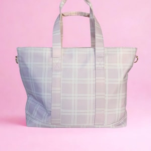May include: A light purple tote bag with a white plaid pattern. The bag has two handles and a shoulder strap. The background is a solid pink color. The bag is made of a soft, durable material.