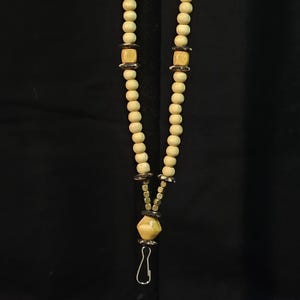 May include: A white wooden beaded lanyard with gold and black accents. The lanyard has a metal clip at the bottom.