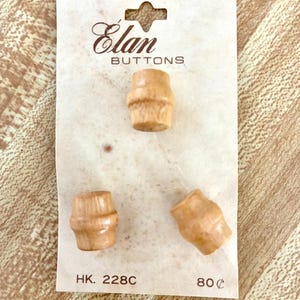 Puede incluir: Tres botones de madera en forma de barril sobre una tarjeta. La tarjeta tiene el texto "Elan BUTTONS" en escritura marrón. Los botones son de color marrón claro y tienen un diseño acanalado. La tarjeta también tiene el texto "HK. 228C".
