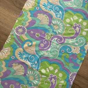 May include: A rectangular fabric piece featuring a vibrant, repeating pattern of swirling paisley shapes, stylized flowers, and geometric motifs. The design incorporates a color palette of bright lime green, light purple, turquoise blue, and soft beige.
