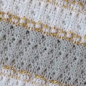 May include: Close-up of a knitted fabric with a white and gray pattern. The fabric has a thin gold thread woven into the design.