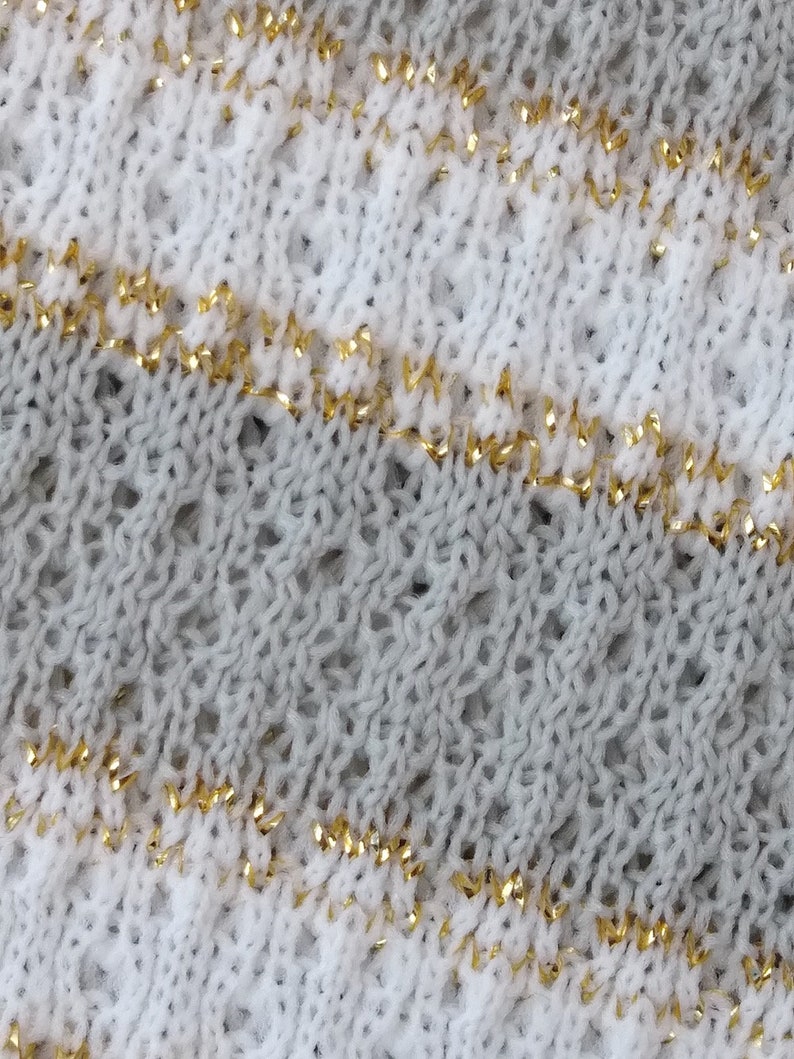 May include: Close-up of a knitted fabric with a white and gray pattern. The fabric has a thin gold thread woven into the design.