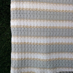 May include: White fabric with horizontal stripes of gold metallic thread. The fabric has a knit texture.