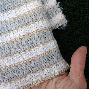 May include: White and gray striped fabric with gold thread woven into the stripes. The fabric has a loose knit texture.