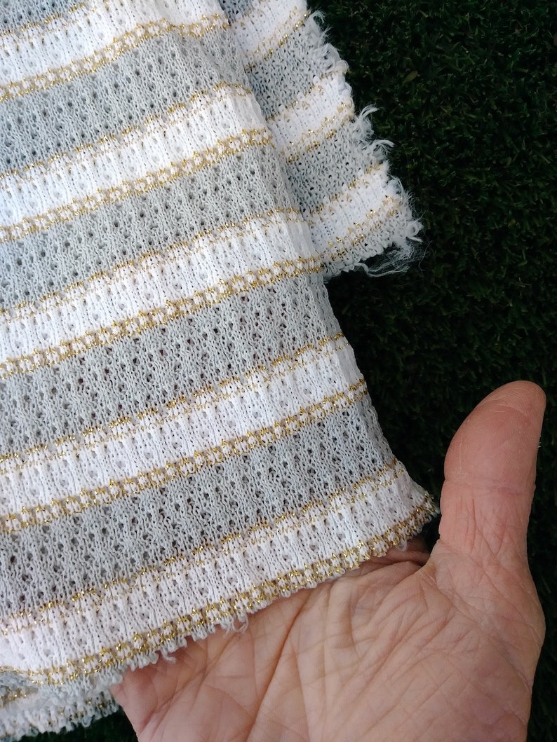 May include: White and gray striped fabric with gold thread woven into the stripes. The fabric has a loose knit texture.