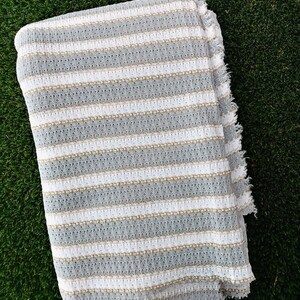 May include: White and gray striped fabric with a textured weave. The fabric has a frayed edge.