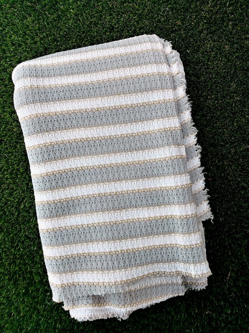 May include: White and gray striped fabric with a textured weave. The fabric has a frayed edge.