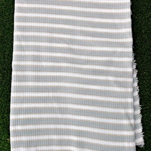 May include: A white and gray striped throw blanket with a textured weave. The blanket has a fringed edge.