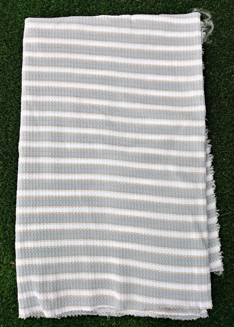 May include: A white and gray striped throw blanket with a textured weave. The blanket has a fringed edge.