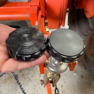 May include: Two black plastic caps with a ridged edge and a circular center. The caps are attached to a metal object.