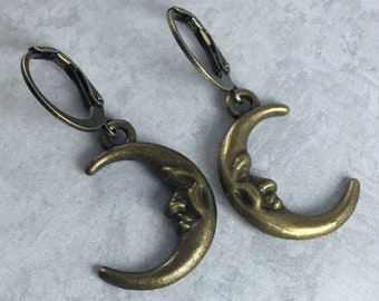 May include: A pair of bronze crescent moon earrings with a face on each moon. The earrings have a simple hook closure.